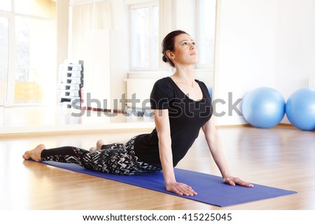 Full length portrait of a middle age woman doing cobra pose on an exercise mat at yoga studio.