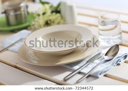 Dinner Place Setting On A Garden Table with Silver Spoon And Knife, Blue Napkin And Plates