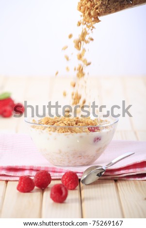 Pouring muesli on a bowl of milk with cereal (muesli/granola) and with fresh strawberries