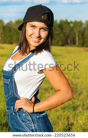 Portrait of a teenage girl in a baseball cap and a denim coveralls in the countryside in summer