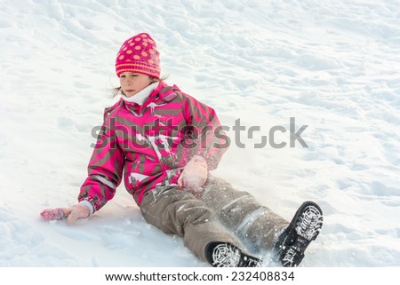 Little girl in bright clothes drives off with snowy hills in winter