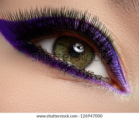 Macro shot of woman\'s beautiful green eye with extremely long eyelashes, bright and deep colors make-up. Dark purple eyeshadow on eyelid. Sexy view, sensual look