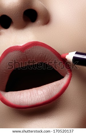 Closeup of woman plump lips with lip liner. Professional make-up artist applying lips liner for perfect make-up contour. Fashion makeup