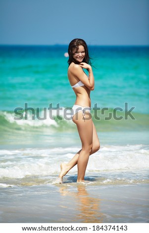 Happy woman in white bikini swimwear walking on a beach. Vacation, beautiful sea and natural. Tan girl in summer. Perfect body shapes, relaxing soul