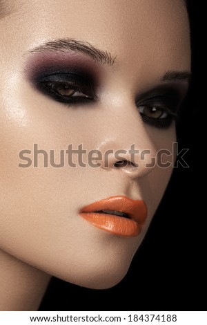 Close-up beauty portrait of attractive model face with bright make-up. Dark smoky eyes makeup, black ad purple eyeshadows, orange lips. Fashion witch style visage for Halloween