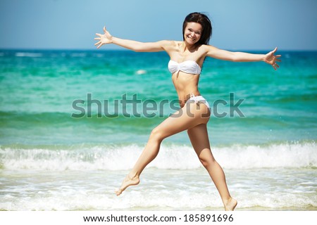 Happy woman in white bikini swimwear open her heart to sun. Vacation, beautiful sea and natural. Tan girl in summer. Perfect body shapes, relaxing soul. Jumping, running, happiness
