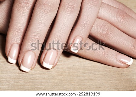 Beautiful woman\'s nails with perfect french manicure on natural wood background. Care for female hands. Natural look with light nail polish, beauty care.