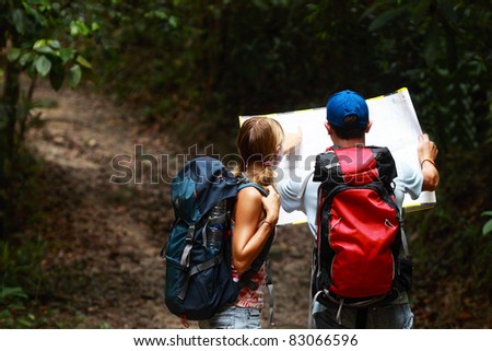 Couple of tourist people looking for a road with map in the dark forest with backpack