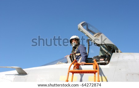 The military pilot in the plane in a helmet in dark blue overalls against the blue sky