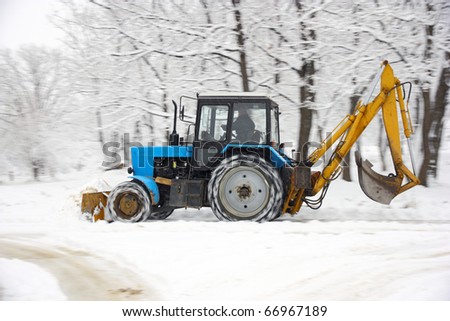 The tractor of dark blue color deletes snow in park
