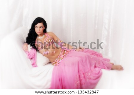 Portrait of beautiful bellydancer wearing a light pink costume and seated in a reclined position.