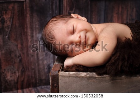 9 day old smiling newborn baby boy sleeping on his stomach in a vintage, weathered wooden crate. Shot in the studio on a rustic, barn wood background.