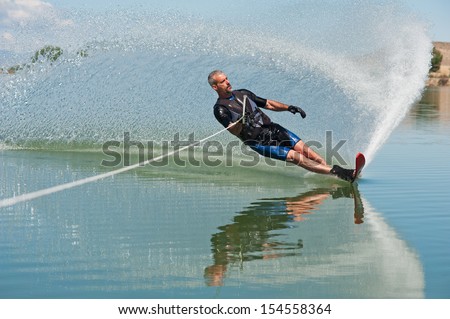 A 50 yr. old man slalom waterskiing on Sweitzer Lake in Delta, Colorado. He is carving the water with his ski as he makes a turn, creating a \