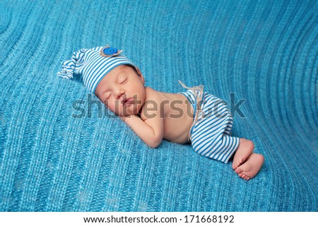 Newborn baby sleeping on a blue blanket and wearing vintage inspired blue and white striped pajamas with matching sleeping cap.