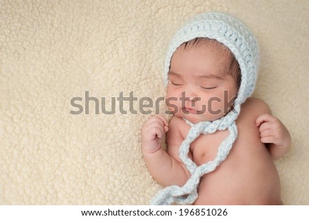 A 7 day old, Hispanic, sleeping baby wearing a light blue, crocheted bonnet. Shot in the studio on a beige blanket.