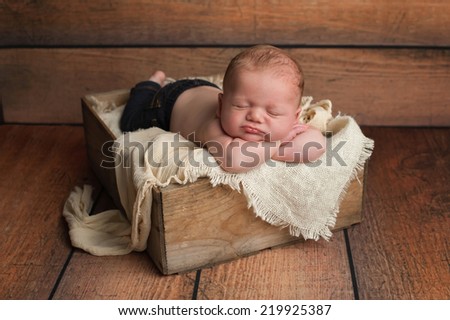 Studio portrait of a 1 month old newborn baby boy wearing jeans and sleeping in a vintage wooden crate.