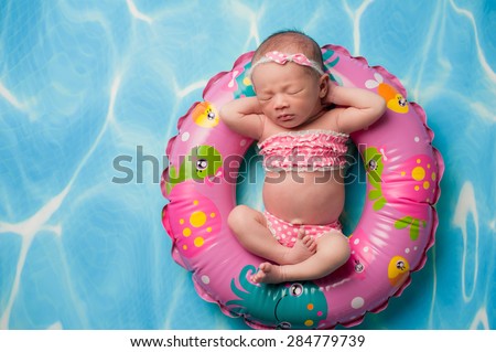 A portrait of a beautiful eleven day old baby girl wearing a pink polka dot bikini. She is sleeping on a pink, inflatable swim ring.