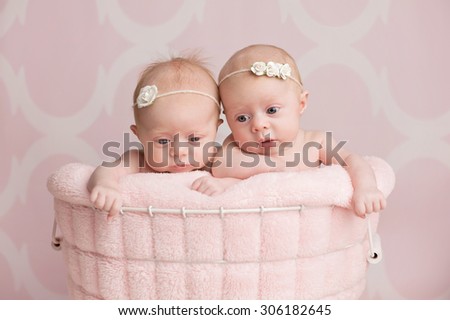 Seven week old, fraternal twin baby girls sitting in a wire basket. Shot in the studio against a pink background.