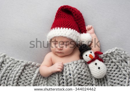 Sleeping, two week old, newborn, baby boy wearing a crocheted Santa hat with snowman plush toy.