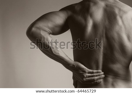 A black and white photo of a muscular man holding his lower back as if experiencing a backache.
