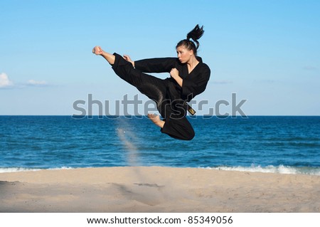 A female, fourth degree, Taekwondo black belt athlete performs a midair jumping kick on the beach.