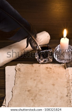 feather, old paper and candle on a wooden background