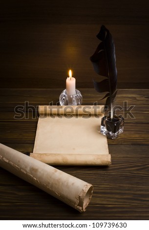 feather, old paper and candle on a wooden background