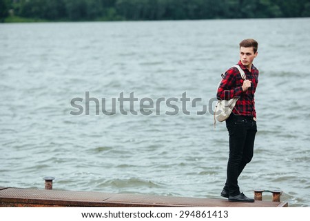 the young man posing on a pier on the background of water