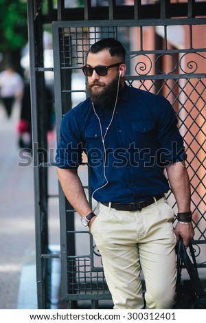 bearded man standing in the street at the bus stop and listen to music