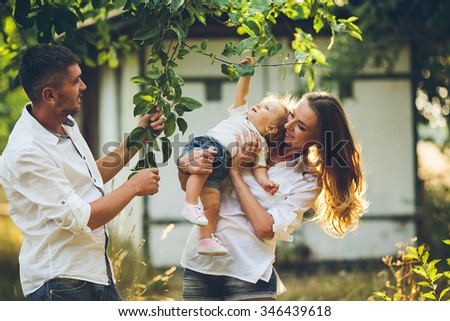 Parents with baby enjoying picnic on a farm with apple and cherry trees.