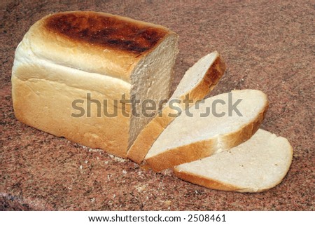 a loaf of freshly baked bread with some slices cut, on a granite worktop