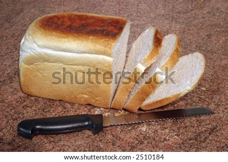a loaf of freshly baked bread with some slices cut, on a granite worktop
