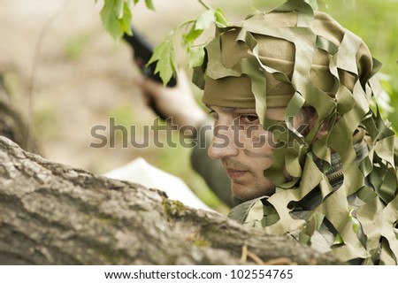Young Camouflaged military man in forest with gun.