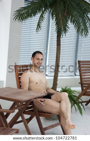 Young Man in tropic resort sitting on wooden chaise lounge