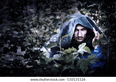 Mystery man in a raincoat with a hood hiding in the trees