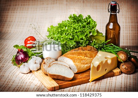 view of vegetables - tomato, green,  garlic, potatoes, lettuce, onion and fresh bread, cheese and glass of milk on old tablecloth