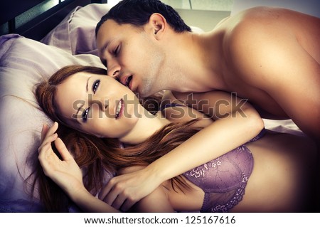 Young man kissing woman in darkness bedroom on bed