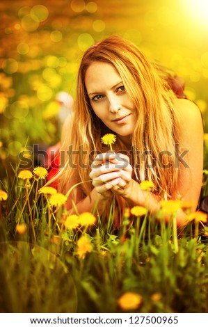 Young beautiful girl student lying on a grass. Summer field with yellow flowers dandelion