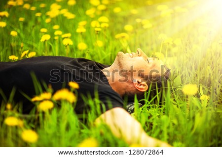 Happy Smiling Man Lying On Grass With Yellow Dandelion At Sunny Day