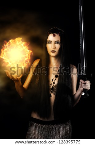 Young sexy woman warrior with long  black hair holding sword and magic fire ball in hands