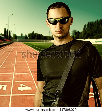 Close-up portrait of a young stylish beautiful man with black sun glasses outdoor at Red treadmill at the stadium