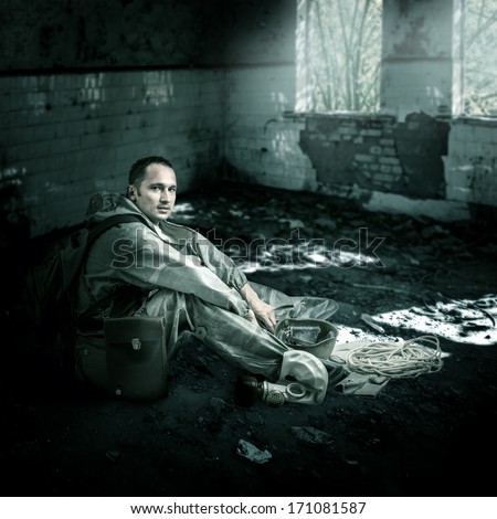 Military man with gas mask sitting on a floor of ruins of buildings in post apocalyptic world