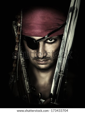 Portrait of handsome male pirate holding sword on black background