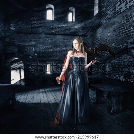 young beautiful female vampire aristocrat with a cup of blood stands in the old castle