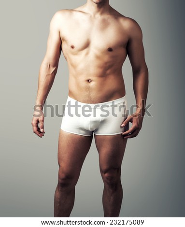 Muscular young sexy handsome man posing in white pants. Male underwear model on gray background
