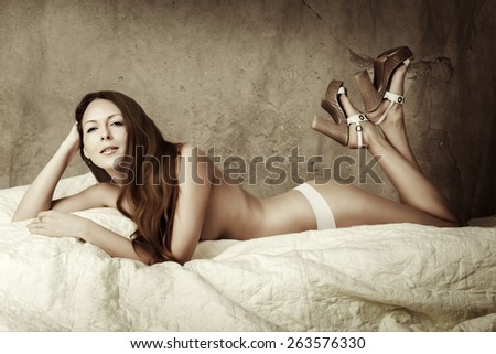 Beautiful slim woman with perfect body and long hair wearing white pants and lying on bed
