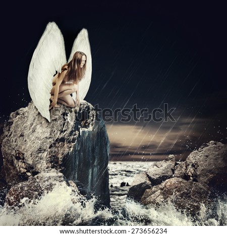 Beautiful sad woman fallen angel with white wings and long hair sitting on a rock about sea