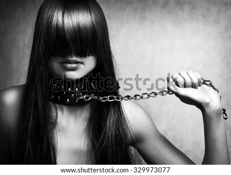 Black and white fashion portrait of young beautiful female model. Glamour woman with long black hair and sexy hairstyle. Lady with leather collar with studs on a metal chain in hand
