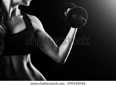 Black and white dark contrast photo of muscular arms, waist and belly with beads of sweat of young fitness woman, which training, working out with dumbbells on black background