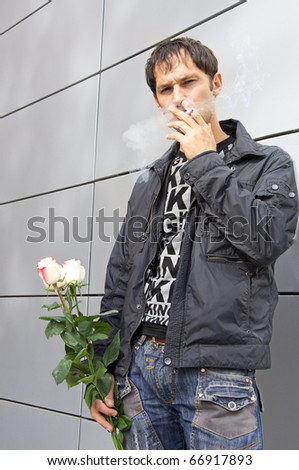 Pretty guy holds three roses in a hand, smokes, looks in the chamber and waits the girl who is late
